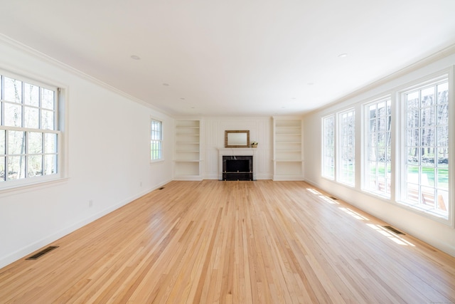 unfurnished living room featuring light wood-style floors, visible vents, built in features, and plenty of natural light