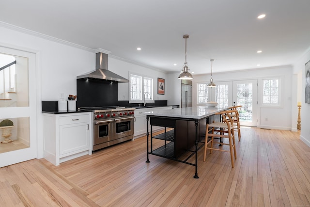 kitchen featuring white cabinetry, crown molding, range with two ovens, light wood-type flooring, and wall chimney exhaust hood