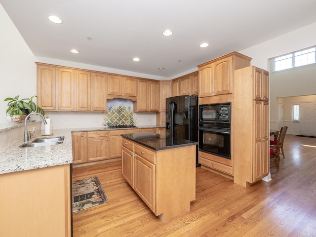 kitchen featuring tasteful backsplash, light stone counters, light brown cabinetry, black appliances, and a sink