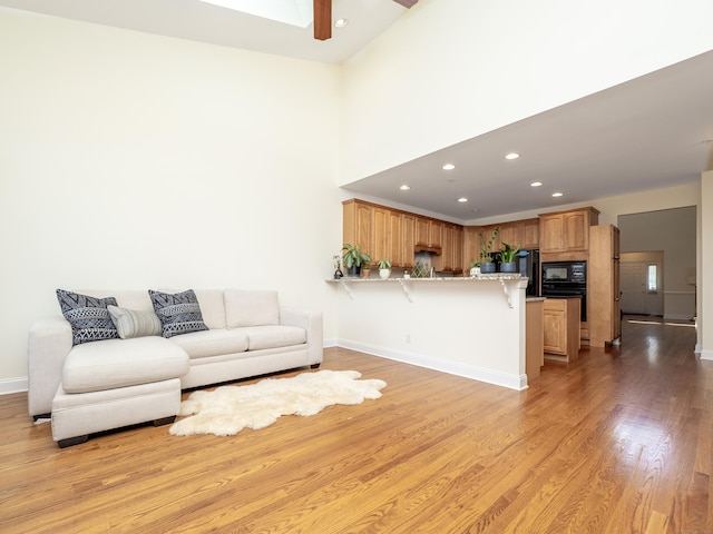 living room with light wood-style floors, ceiling fan, baseboards, recessed lighting, and a high ceiling