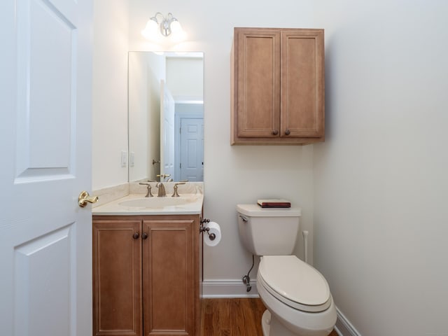 half bath with baseboards, wood finished floors, toilet, and vanity