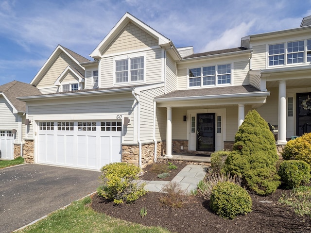 view of front of home with covered porch, a shingled roof, driveway, and stone siding