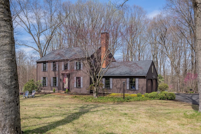 colonial inspired home with a shingled roof, a chimney, and a front yard