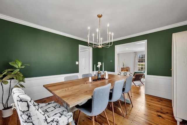 dining area featuring hardwood / wood-style floors, a wainscoted wall, a chandelier, and ornamental molding