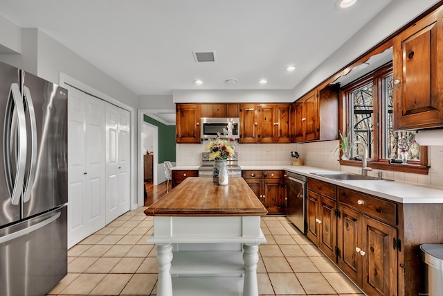 kitchen featuring light tile patterned flooring, decorative backsplash, stainless steel appliances, and a sink