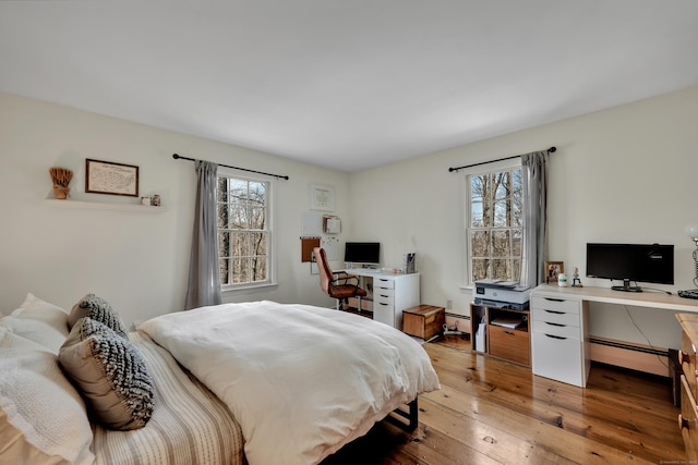 bedroom with a baseboard heating unit and light wood-style flooring