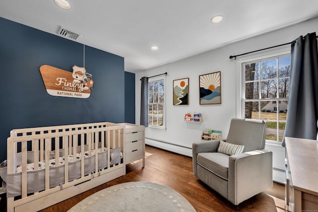 bedroom featuring recessed lighting, a crib, wood finished floors, visible vents, and baseboard heating