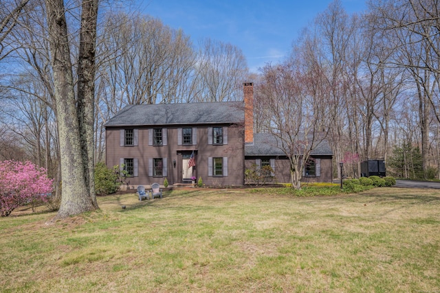 colonial house featuring a chimney, a front lawn, and roof with shingles