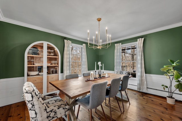 dining area with a wainscoted wall, a notable chandelier, and crown molding