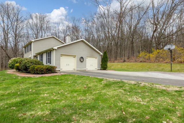 view of side of home featuring a yard, an attached garage, driveway, and a chimney