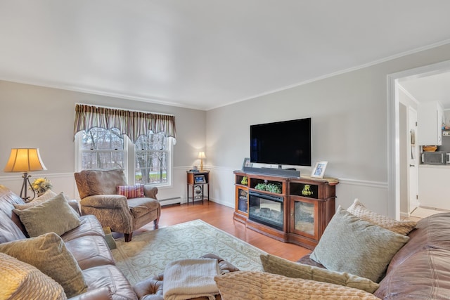 living area featuring crown molding, wood finished floors, baseboard heating, and a wainscoted wall