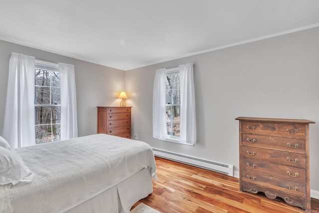 bedroom with ornamental molding, wood finished floors, baseboard heating, and multiple windows