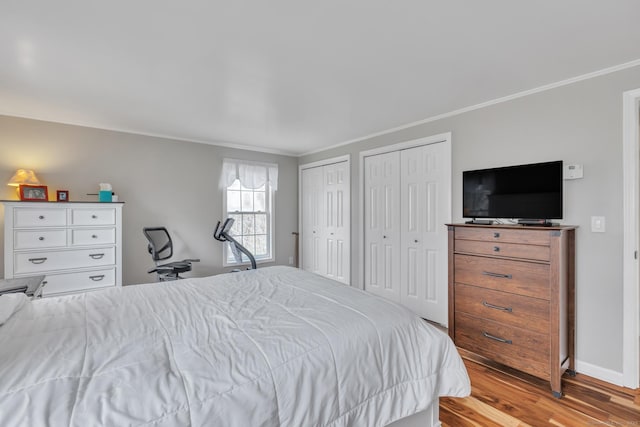 bedroom featuring baseboards, multiple closets, ornamental molding, and wood finished floors
