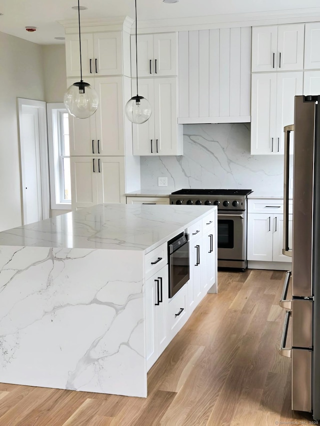 kitchen featuring appliances with stainless steel finishes, decorative backsplash, pendant lighting, light wood-type flooring, and white cabinets