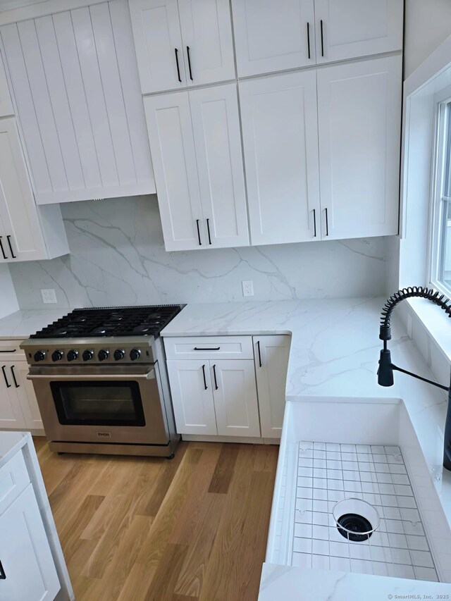 kitchen with stainless steel stove, light wood-type flooring, white cabinets, and tasteful backsplash