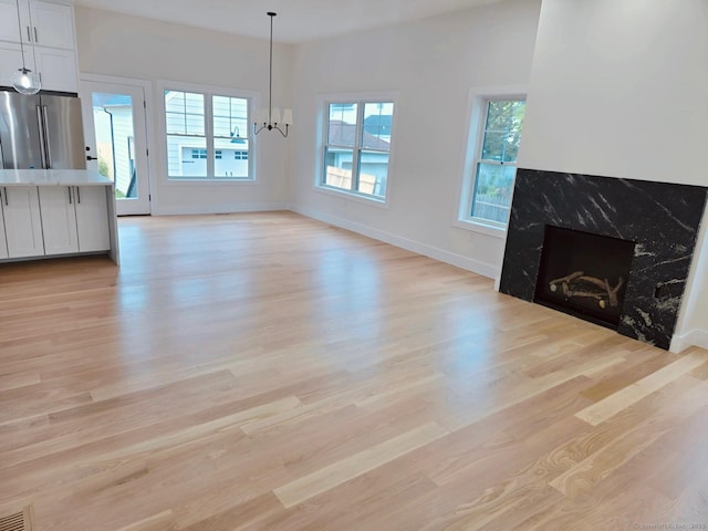 unfurnished living room featuring light wood-style flooring, baseboards, a chandelier, and a premium fireplace