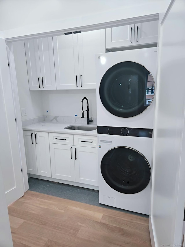 clothes washing area featuring stacked washer and clothes dryer, cabinet space, and light wood-style flooring