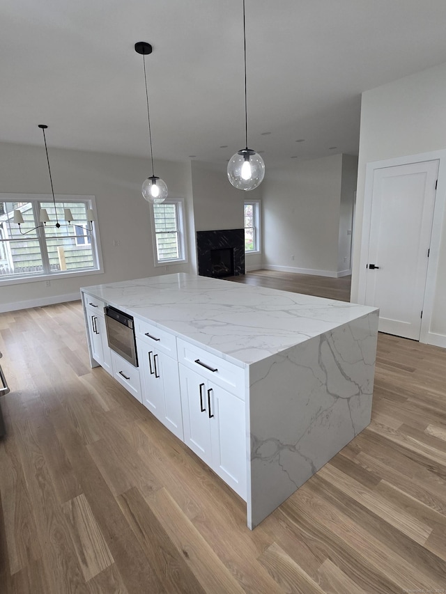 kitchen with light wood-type flooring, a premium fireplace, a kitchen island, white cabinets, and light stone countertops