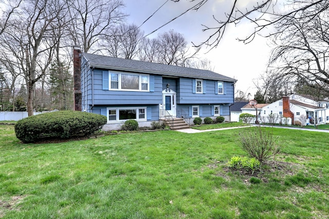 bi-level home featuring a chimney, a front lawn, and fence