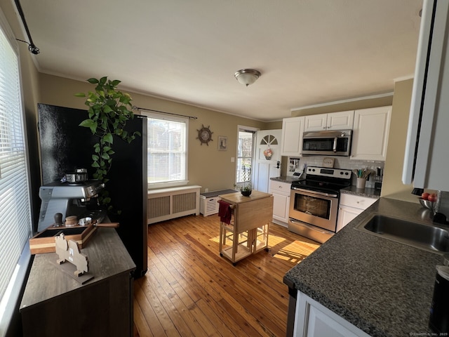 kitchen with ornamental molding, radiator heating unit, a sink, dark countertops, and stainless steel appliances