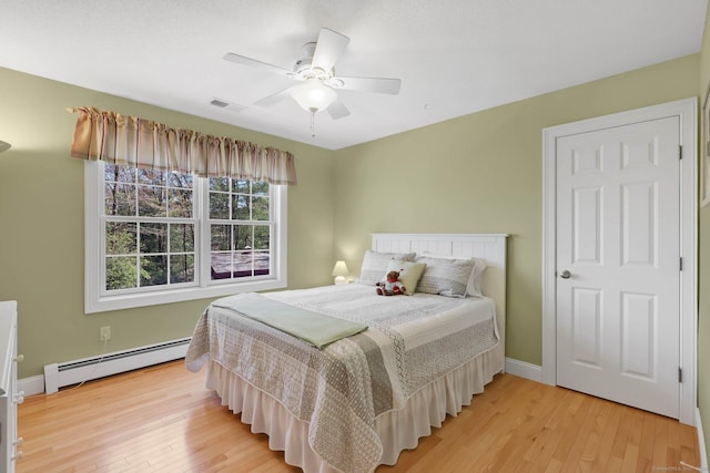 bedroom with a ceiling fan, visible vents, baseboard heating, baseboards, and light wood finished floors