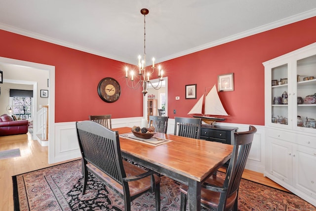 dining area with crown molding, a wainscoted wall, an inviting chandelier, and light wood finished floors