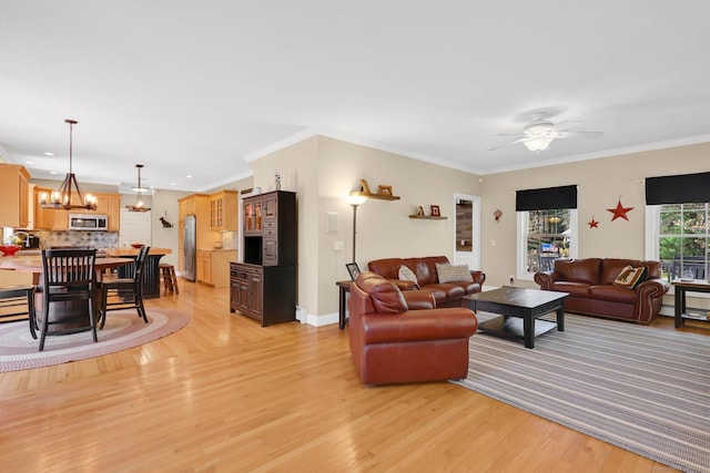 living room featuring baseboards, ornamental molding, ceiling fan with notable chandelier, and light wood finished floors
