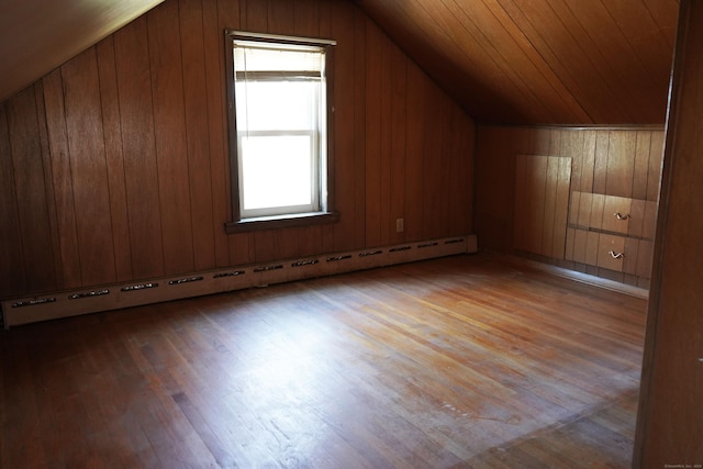 additional living space featuring a baseboard heating unit, hardwood / wood-style flooring, wood walls, and lofted ceiling