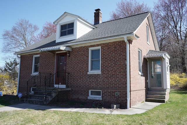 view of front of property with a chimney, a front lawn, entry steps, brick siding, and roof with shingles