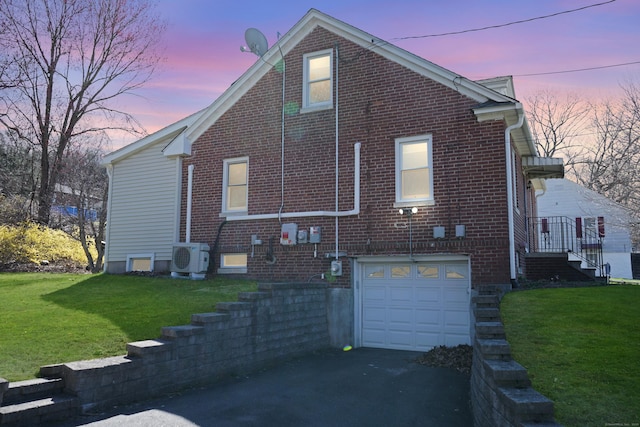 view of home's exterior with driveway, brick siding, an attached garage, a lawn, and ac unit