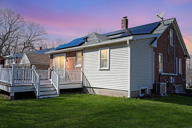 rear view of property featuring a chimney, solar panels, a lawn, brick siding, and a deck