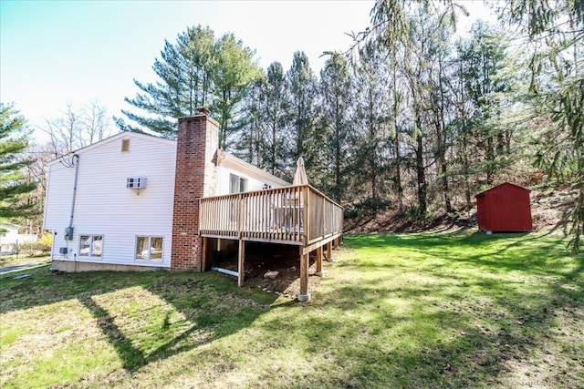 rear view of property featuring a chimney, a storage shed, a wooden deck, an outdoor structure, and a lawn