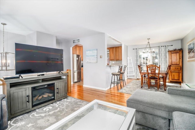 living room with arched walkways, light wood-style floors, baseboards, and an inviting chandelier