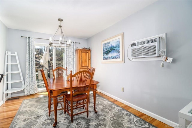 dining area featuring baseboards, a notable chandelier, light wood-type flooring, and a wall unit AC
