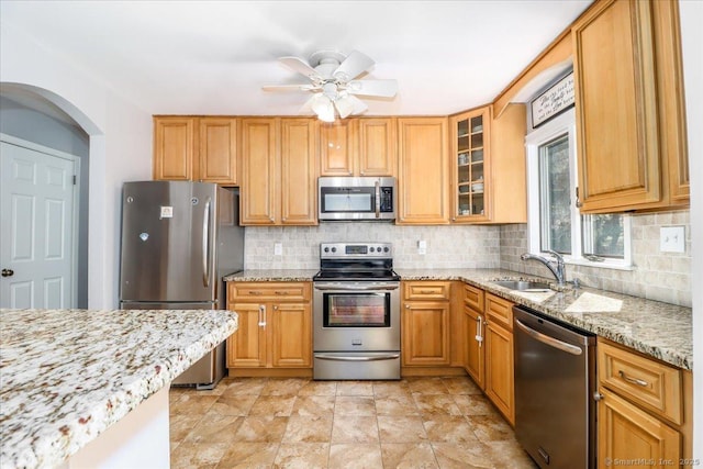 kitchen featuring light stone counters, a sink, ceiling fan, arched walkways, and stainless steel appliances