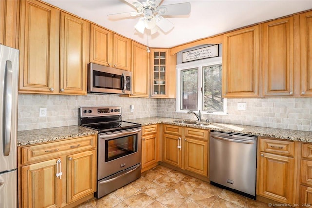 kitchen featuring light stone countertops, appliances with stainless steel finishes, ceiling fan, and a sink