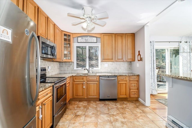 kitchen with a sink, backsplash, ceiling fan, light stone countertops, and appliances with stainless steel finishes