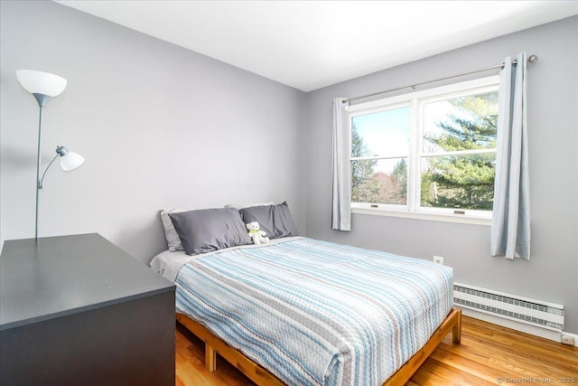 bedroom featuring a baseboard radiator, baseboards, and light wood-type flooring