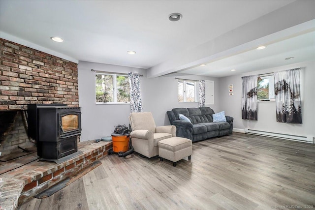 living room with wood finished floors, a baseboard heating unit, a wood stove, baseboards, and recessed lighting