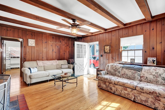 living room featuring a ceiling fan, radiator heating unit, wood finished floors, wood walls, and beam ceiling
