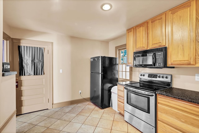 kitchen featuring light brown cabinets, light tile patterned flooring, dark stone counters, baseboards, and black appliances