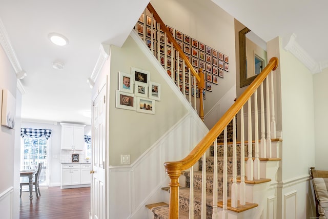 staircase with wood finished floors, a decorative wall, and ornamental molding