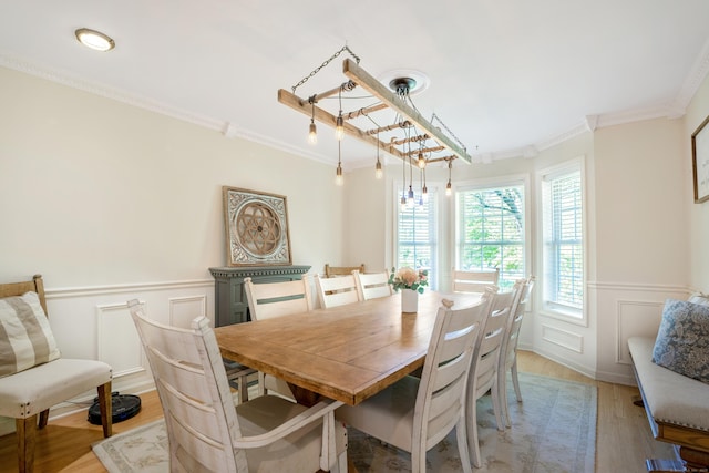 dining room featuring light wood finished floors, crown molding, a wainscoted wall, and a decorative wall