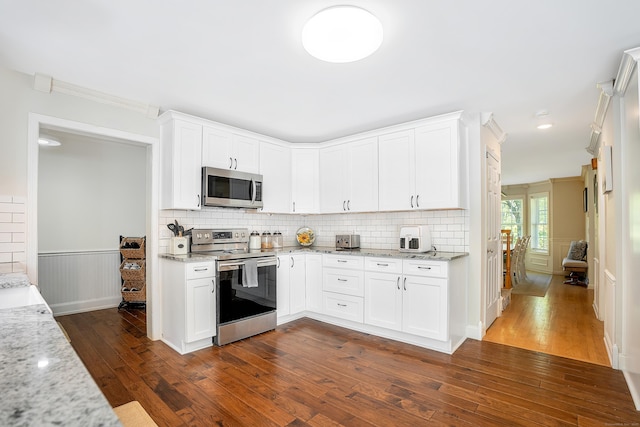 kitchen with stainless steel appliances, dark wood finished floors, light stone counters, white cabinetry, and a wainscoted wall
