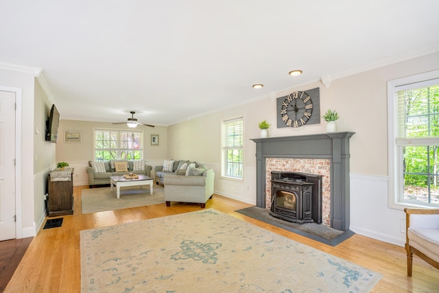 living room with wood finished floors, plenty of natural light, crown molding, a ceiling fan, and a wainscoted wall