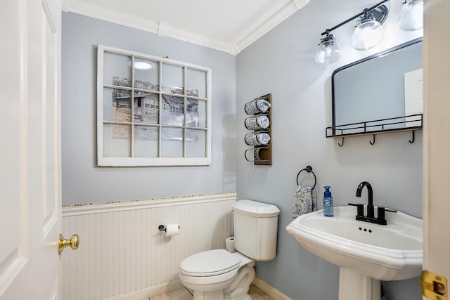 bathroom with crown molding, a sink, toilet, and a wainscoted wall