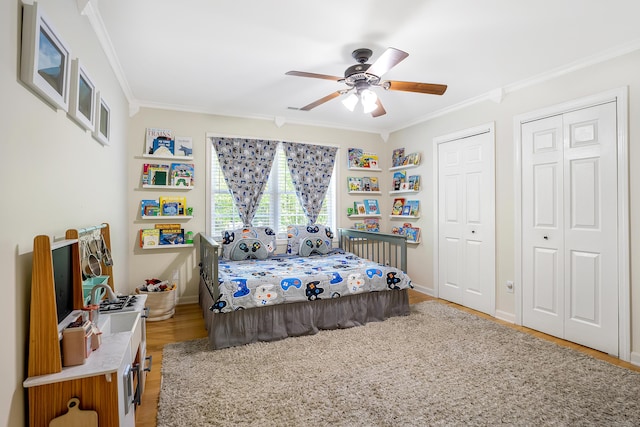 bedroom with ornamental molding, light wood-style flooring, two closets, and a ceiling fan