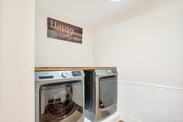 laundry room featuring washing machine and clothes dryer, ornamental molding, and wainscoting