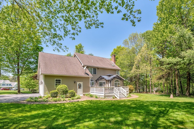 rear view of house featuring driveway, a yard, a deck, and a chimney