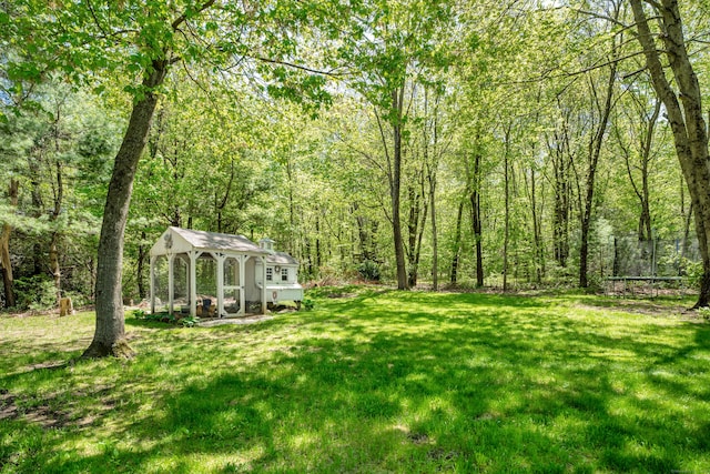 view of grassy yard with exterior structure, a trampoline, an outbuilding, and a wooded view